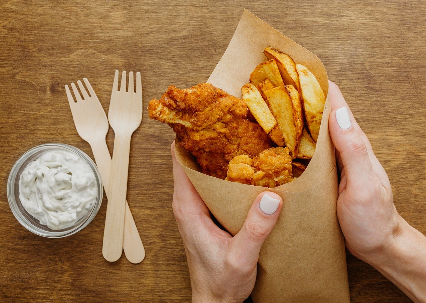 Top view of fish and chips in paper wrap held by woman